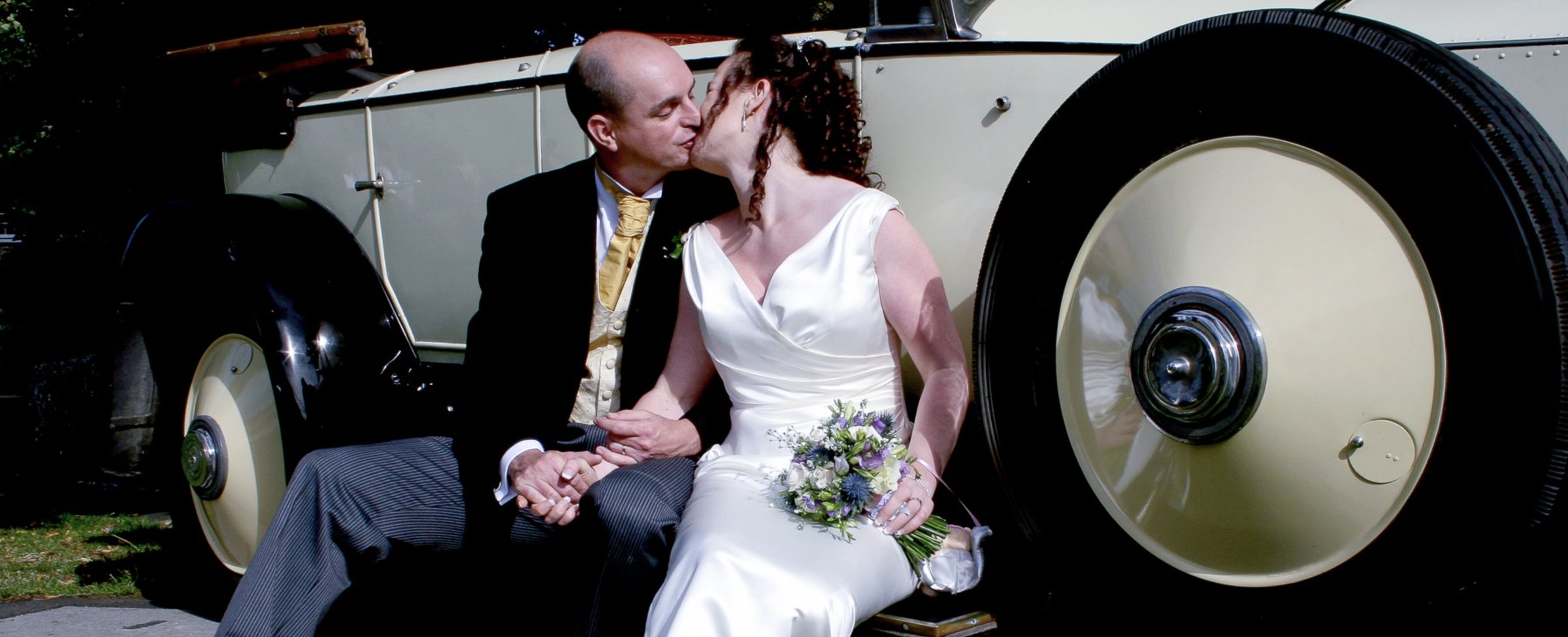 Bride and groom kissing beside a vintage car
